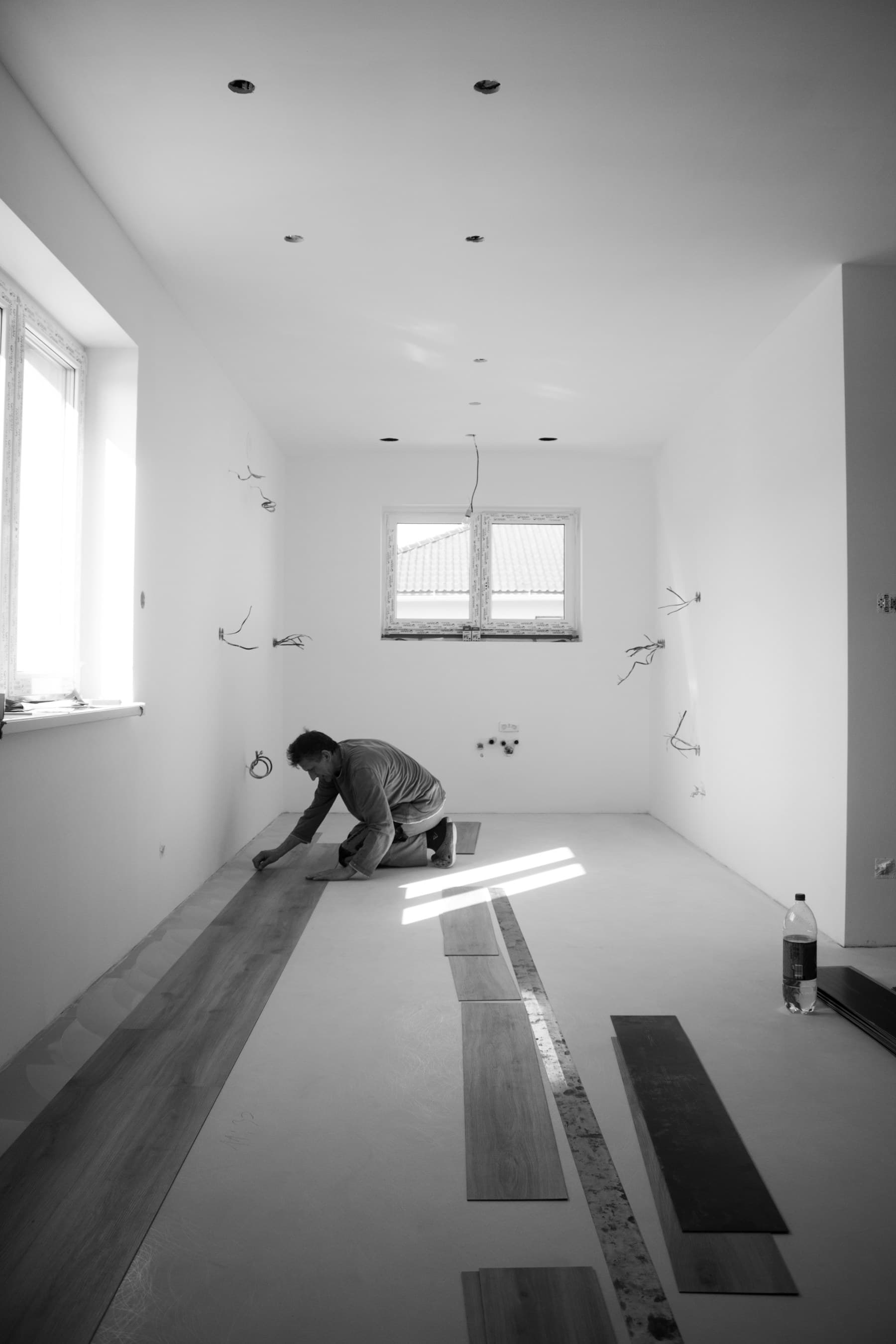 Fitter kneeling to lay an engineered oak board against a skirting line.